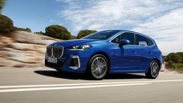 BMW 2 серії Active Tourer 230e плагін-гібрид U06 2021, в русі на дорозі серед сільської місцевості Плагін-гібрид BMW 2 Series Active Tourer 230e U06 2021 M у кольорі Portimao Blue металік, вид збоку в три чверті, в русі на дорозі
