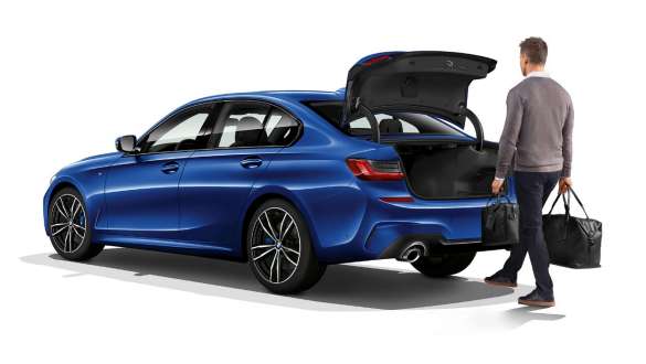 BMW 3 серії Седан, функція автоматичного відкривання кришки багажного відділення. Знімок ззаду BMW 3 серії Седан з водієм, який автоматично відкриває кришку багажника ногою, три чверті.