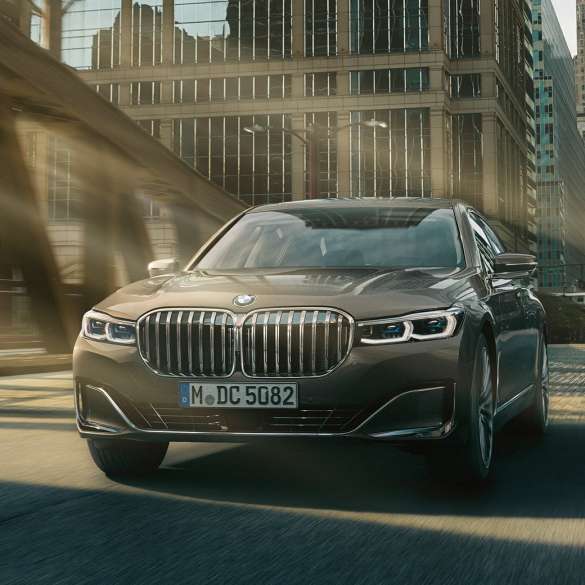 BMW 7 серії Седан: системи допомоги водієві Системи допомоги водієві: BMW 7 серії Седан в русі на тлі міського пейзажу