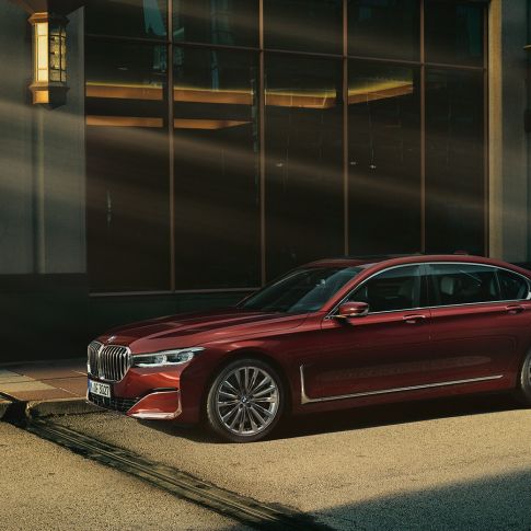 BMW 7 серии Седан Individual: вид збоку BMW 7 серії Седан Individual червоного кольору: вид збоку на тлі міського пейзажу