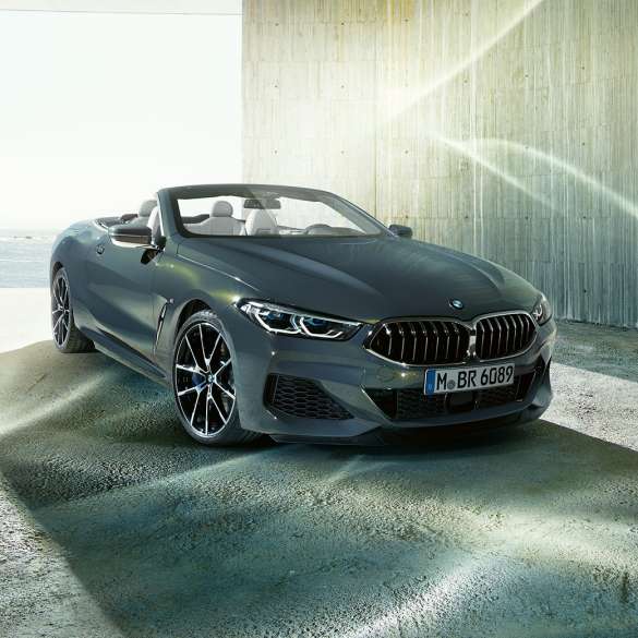 BMW M850i xDrive Кабріолет, вид спереду з поворотом в три чверті. BMW M850i xDrive Кабріолет в Dravit Grey металік з відкритим м'яким верхом, вид спереду з поворотом в три чверті, на березі.