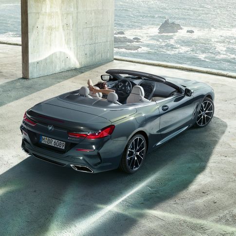 BMW M850i xDrive Кабріолет, з висоти пташиного польоту. BMW M850i xDrive Кабріолет в Dravit Grey металік з відкритим м'яким верхом, з висоти пташиного польоту, паркування в бетонній будівлі перед океаном.