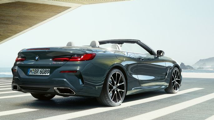 BMW M850i xDrive Кабріолет, вид ззаду з поворотом в три чверті. BMW M850i xDrive Кабріолет в Dravit Grey металік з відкритим м'яким верхом, вид ззаду з поворотом в три чверті, паркування перед океаном.