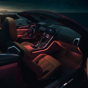 Салон BMW M8 Competition Кабріолет. BMW M8 Competition Кабріолет з відкритим м'яким дахом, салон з червоним фоновим освітленням уночі.