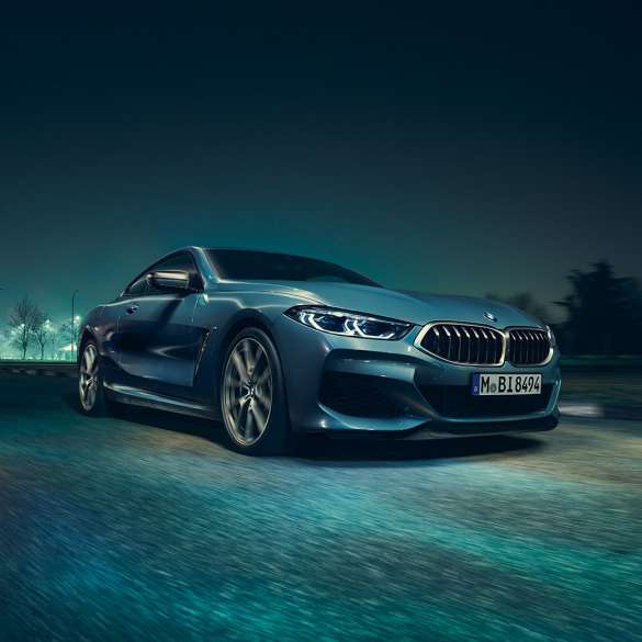 BMW M850i xDrive Coupé, вид спереду з поворотом в три чверті зліва. BMW M850i xDrive Coupé в Barcelona Blue металік, вид спереду з поворотом в три чверті зліва, їзда вночі.