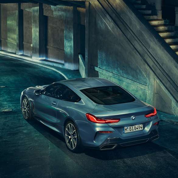 BMW M850i xDrive Coupé, вид ззаду з поворотом в три чверті зліва. BMW M850i xDrive Coupé в Barcelona Blue металік, вид ззаду з поворотом в три чверті ліворуч, стоїть вночі.