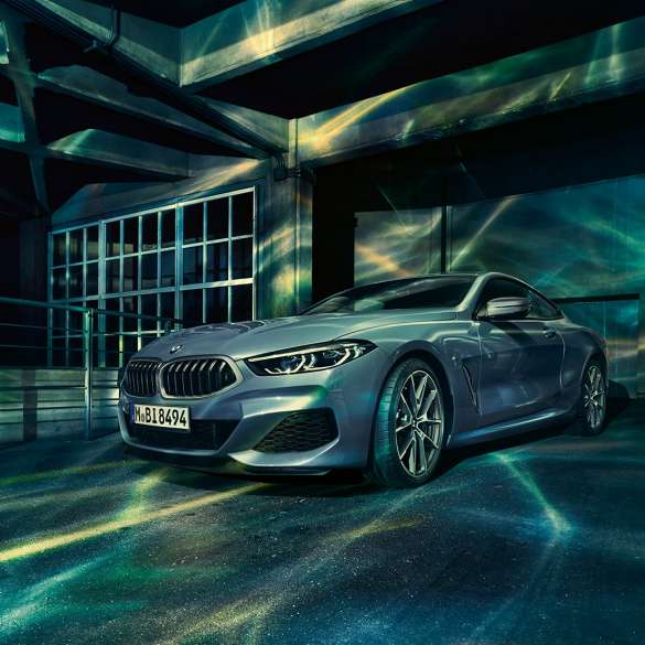 BMW M850i xDrive Coupé, вид спереду з поворотом в три чверті. BMW M850i xDrive Coupé в Barcelona Blue металік, вид спереду з поворотом в три чверті, перед будівлею.