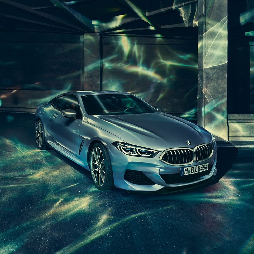 BMW M850i xDrive, вид спереду з поворотом в три чверті зліва. BMW M850i xDrive Coupé в Barcelona Blue металік, вид спереду з поворотом в три чверті зліва, стоїть перед будівлею.