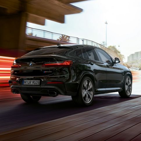 BMW X4 M40i, вид ззаду з поворотом в три чверті. BMW X4 M40i в Black Sapphire металік, екстер'єр, вид ззаду з поворотом в три чверті, права сторона зі світловими смужками.