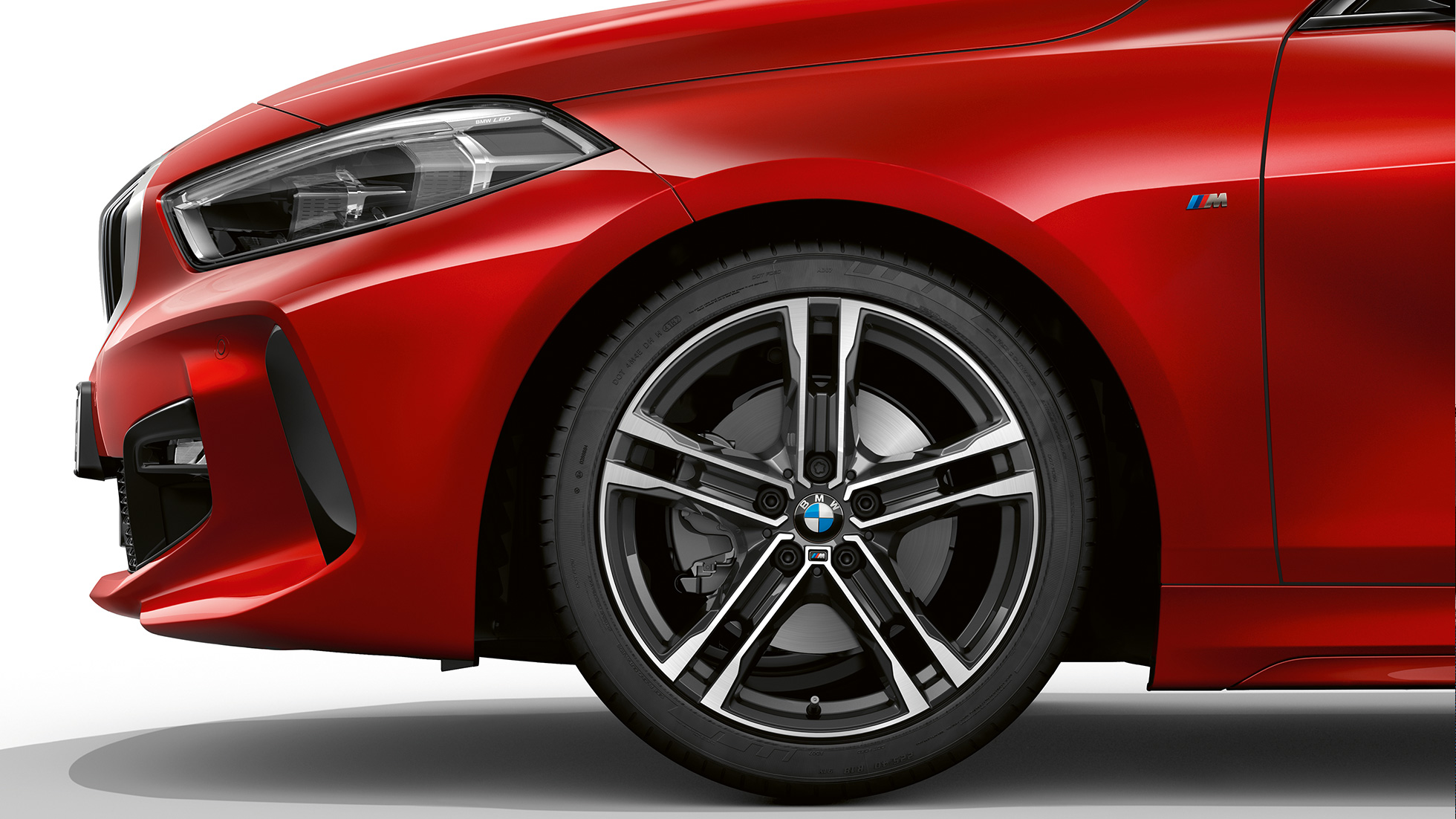 BMW 1 серії модель M Sport, спереду збоку. BMW 1 серії модель M Sport в Melbourne Red металік, спереду збоку з 17-дюймовими легкосплавними дисками M з подвійними спицями, стиль 550 M, двоколірні.