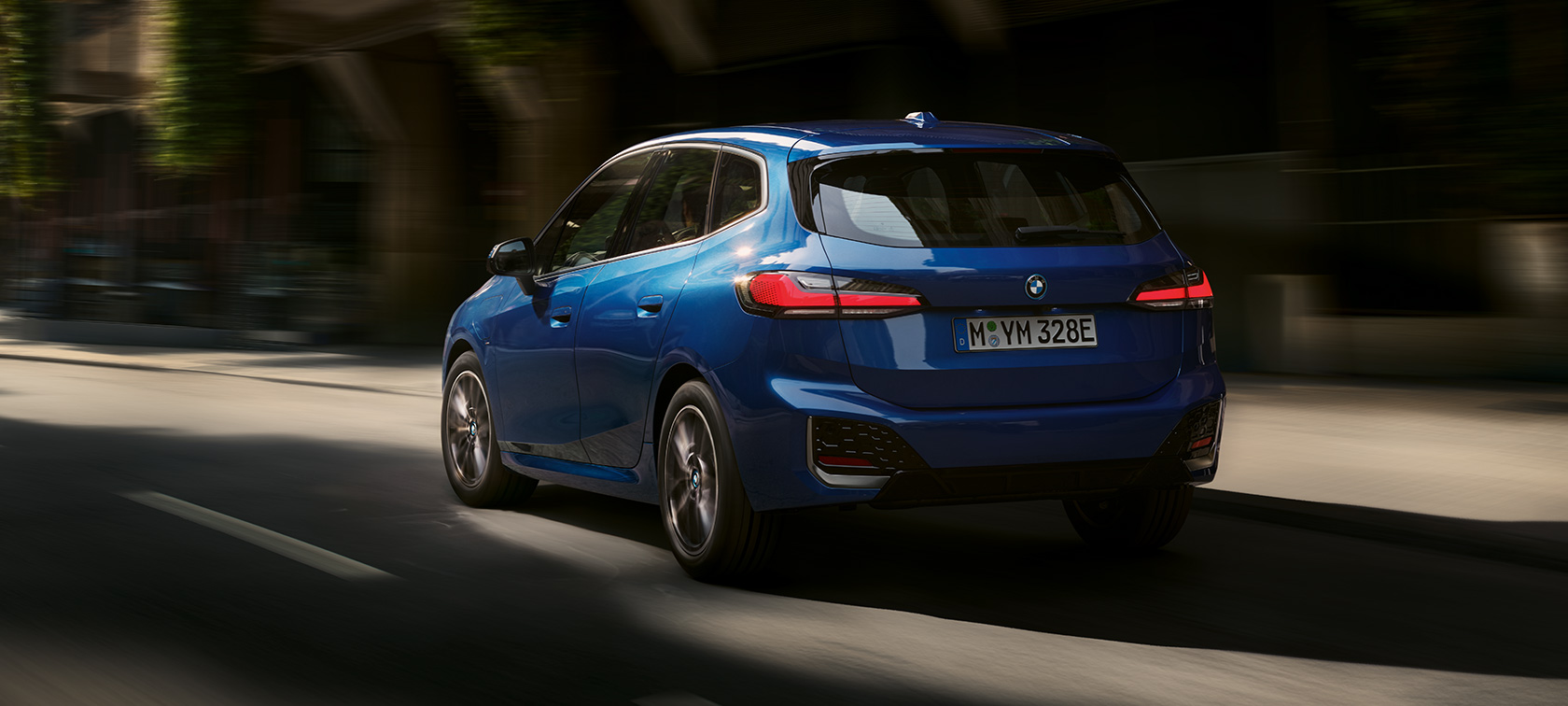 Плагін-гібрид BMW 2 серії Active Tourer 230e U06 2021 M у кольорі Portimao Blue металік, вид у три чверті ззаду, в русі серед міста