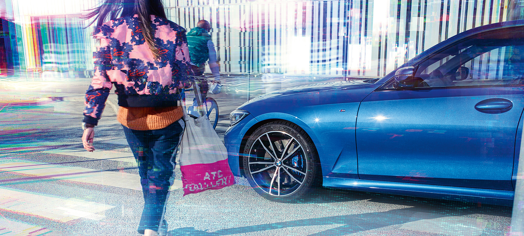 BMW 3 серії Седан, бічний знімок, три чверті. Боковий знімок седана BMW 3 серії на асфальті на міському тлі з пасажирами з поворотом в три чверті.
