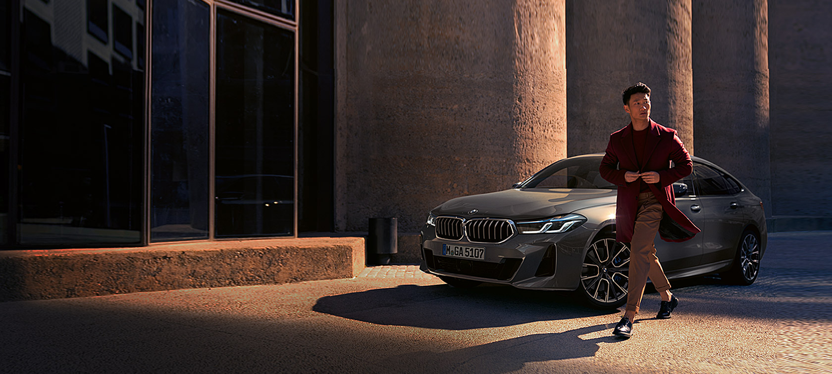 BMW 6 серії Gran Turismo 640i xDrive G32 2020 у кольорі Bernina Grey з чоловіком, що стоїть перед машиною, вид на три чверті спереду