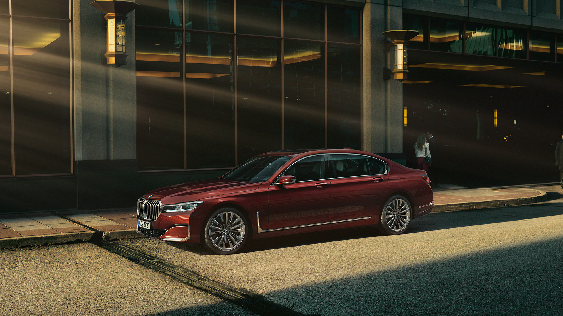 BMW 7 серии Седан Individual: вид збоку BMW 7 серії Седан Individual червоного кольору: вид збоку на тлі міського пейзажу