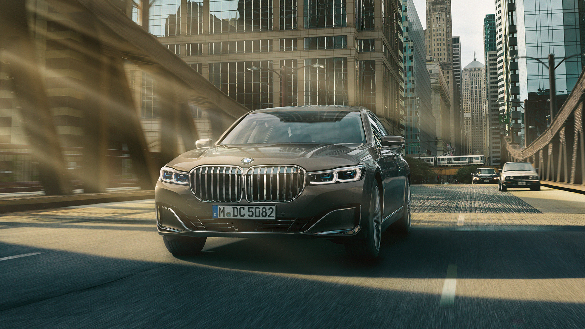 BMW 7 серії Седан: системи допомоги водієві Системи допомоги водієві: BMW 7 серії Седан в русі на тлі міського пейзажу