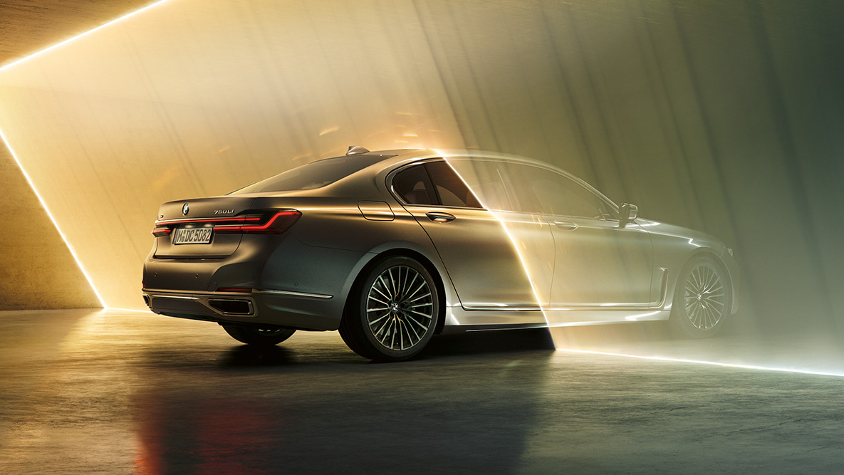 BMW 7 серії Седан кольору «Bernina Grey» BMW 7 серії Седан: автомобіль кольору «Bernina Grey», вид ззаду з поворотом в три чверті в оточенні потоків світла