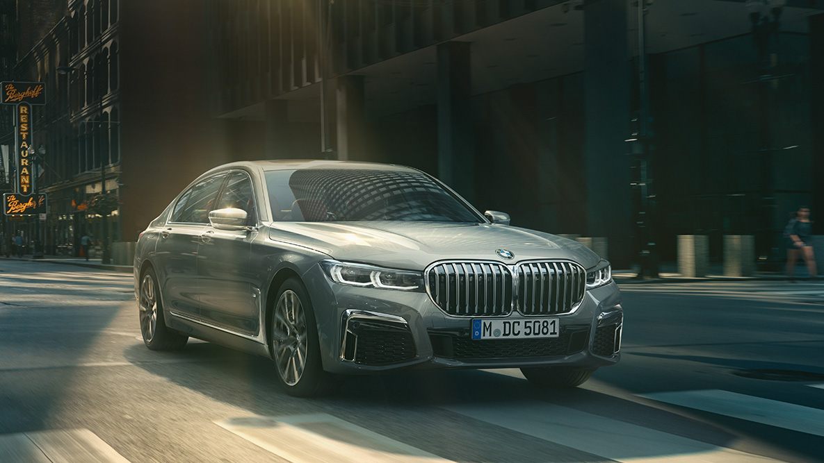 Пакет систем допомоги водієві Driving Assistant Professional седану BMW 7 серії Асистент керування Professional: BMW 7 серії Седан в русі на тлі міського пейзажу, вид спереду з поворотом в три чверті