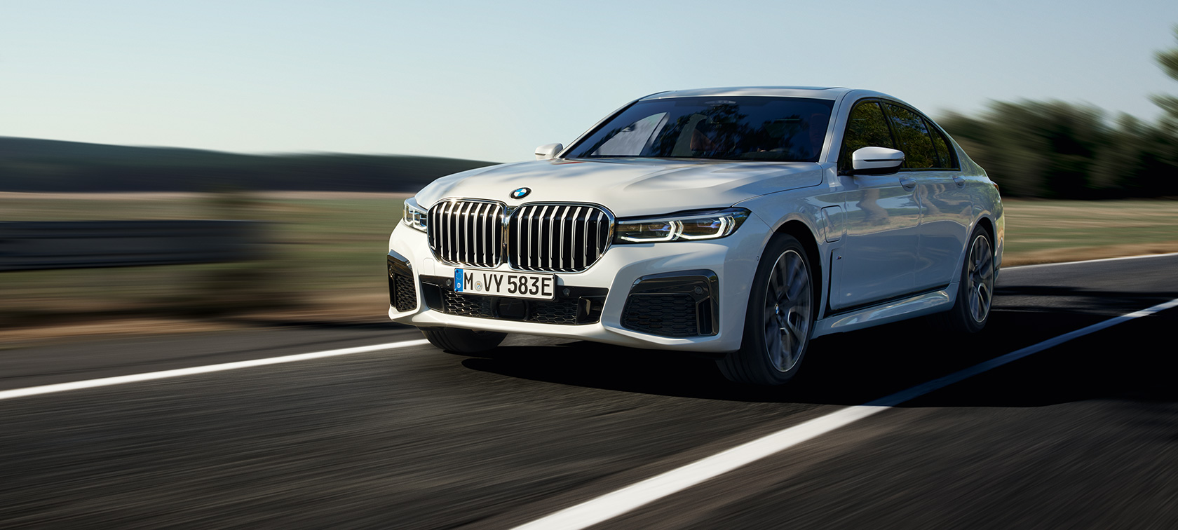 BMW 745e Седан плагин гибрид G11 G12 в цвете Mineral White, вид спереди на три четверти BMW 745e Седан плагин гибрид G11 G12 в цвете Mineral White metallic на грунтовой дороге, вид на три четверти спереди
