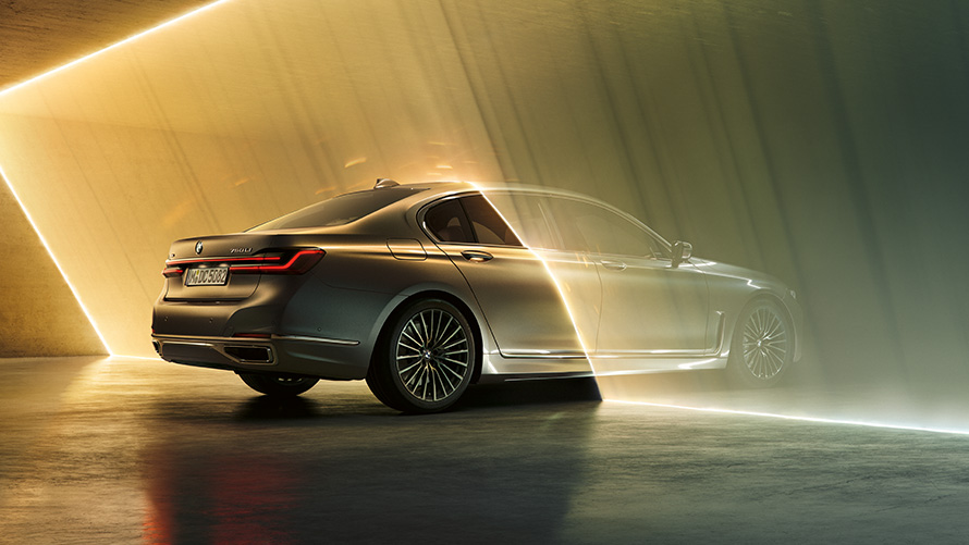 BMW 7 серии G11 G12 2021 технические характеристики BMW 750Li xDrive Седан G11 G12 2019 в цвете Bernina Grey Amber Effect, вид на освещенную лучем света машину, три четверти ззади