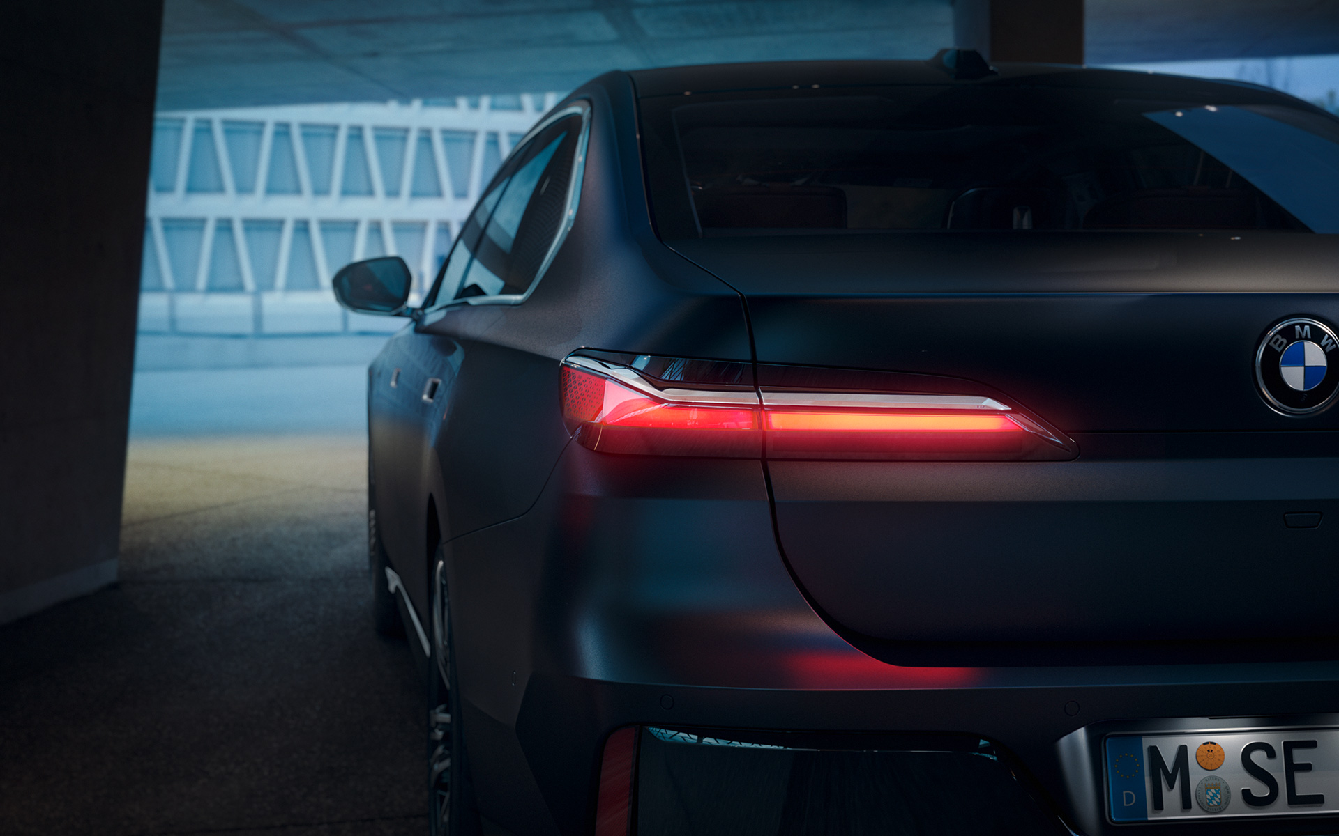 Вигляд ззаду BMW 7 серії Седан G70 ICE в пакеті 740i M Sport, Frozen Deep gray metalliс BMW 7 серії Седан G70 ICE 740i пакет M Sport, Frozen Deep gray metalliс, вид ззаду з увімкненими задніми ліхтарями