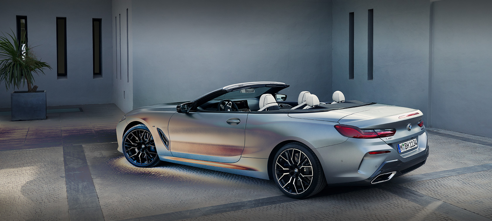 Чоловік опирається на BMW 8 Series Convertible G14 LCI Facelift 2022 у кольорі BMW Individual Frozen Pure Grey, вид збоку, на фоні будівлі