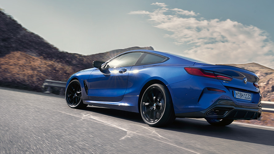 BMW 8 серії Coupe G15 LCI Facelift, вид ззаду в три чверті під час руху BMW 8 серії Coupe М у кольорі Portimao Blue metallic G15 LCI Facelift, вид ззаду на три чверті під час руху на фоні пагорбів