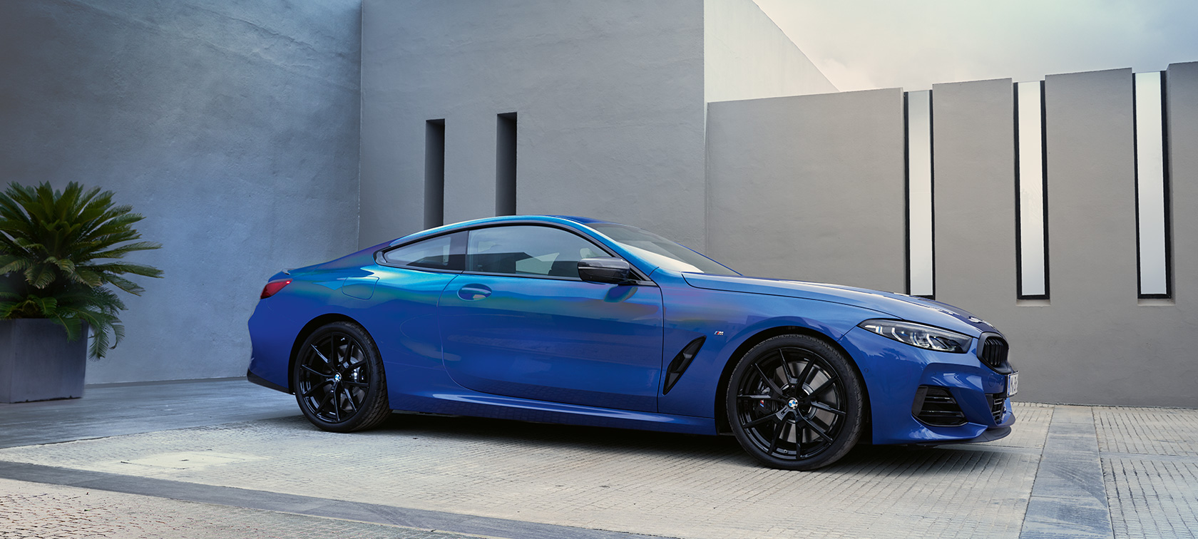 BMW 8-series Coupe G15 LCI Facelift 2022 M у кольорі Portimao Blue metallic, вигляд збоку на фоні стіни будинку