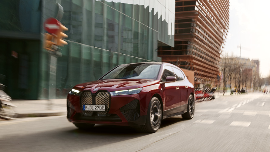 BMW iX i20 електричний кросовер BMW iX xDrive50 системи допомоги водієві BMW iX i20 2021 електричний кросовер BMW iX xDrive50 у кольорі Aventurin Red їде околицями міста
