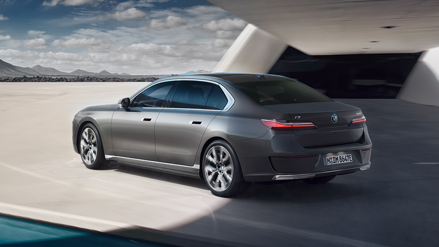BMW i7 Седан, вид три чверті ззаду BMW i7 Седан G70 у кольорі BMW Individual Oxid grey metallic, вид три чверті на фоні будівлі