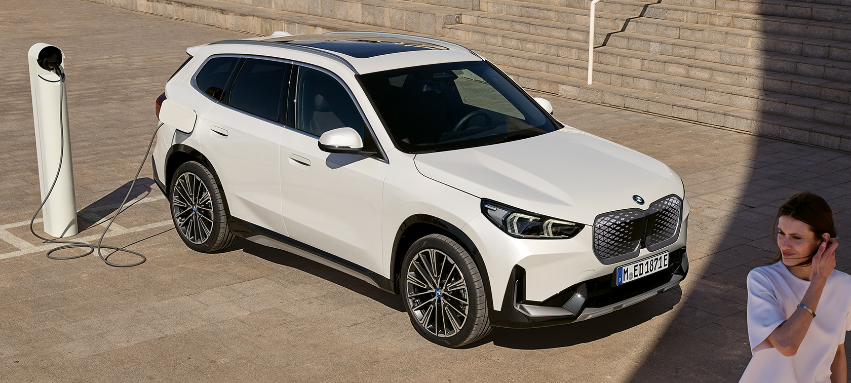 BMW iX1 U11 BEV, вид збоку під час заряджання BMW iX1 U11 BEV 2022 у кольорі Mineral White metallic, вид збоку з поворотом у дві треті під час заряджання