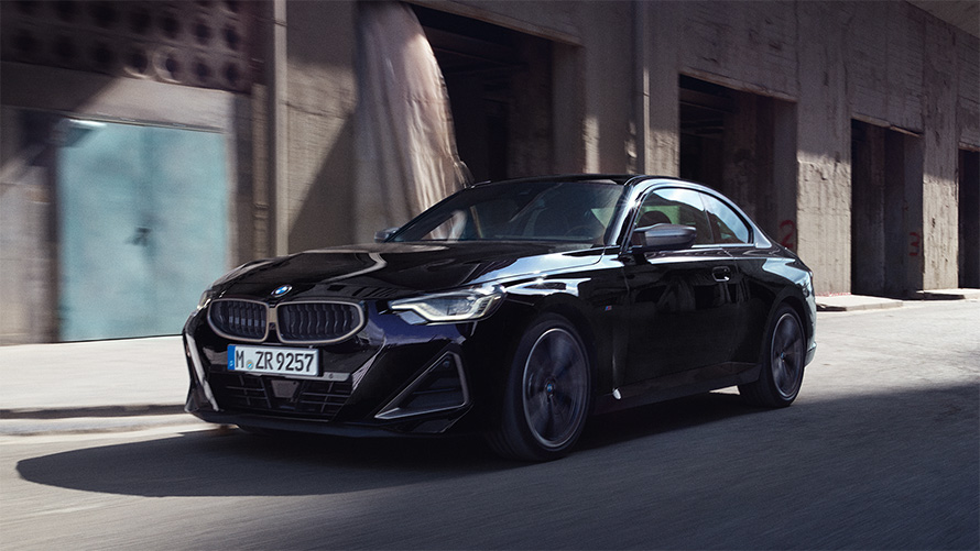 BMW M240i xDrive Coupé G42 2021 у кольорі Black Sapphire металік, вид спереду в три чверті в русі навпроти складу