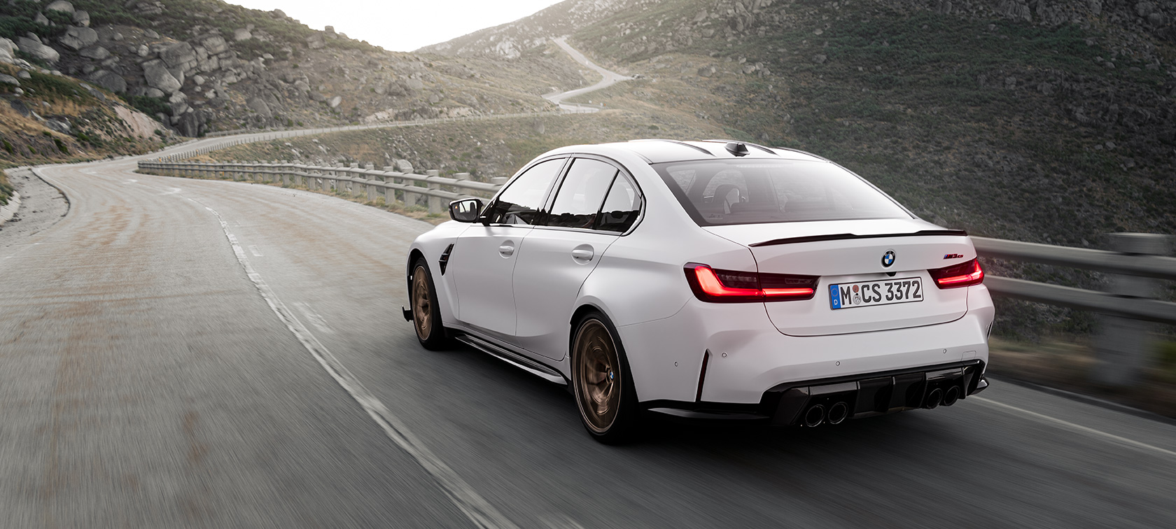 BMW M3 CS G80, вид ззаду в три чверті в русі BMW M3 CS G80, вид ззаду в три чверті в русі на гірській дорозі