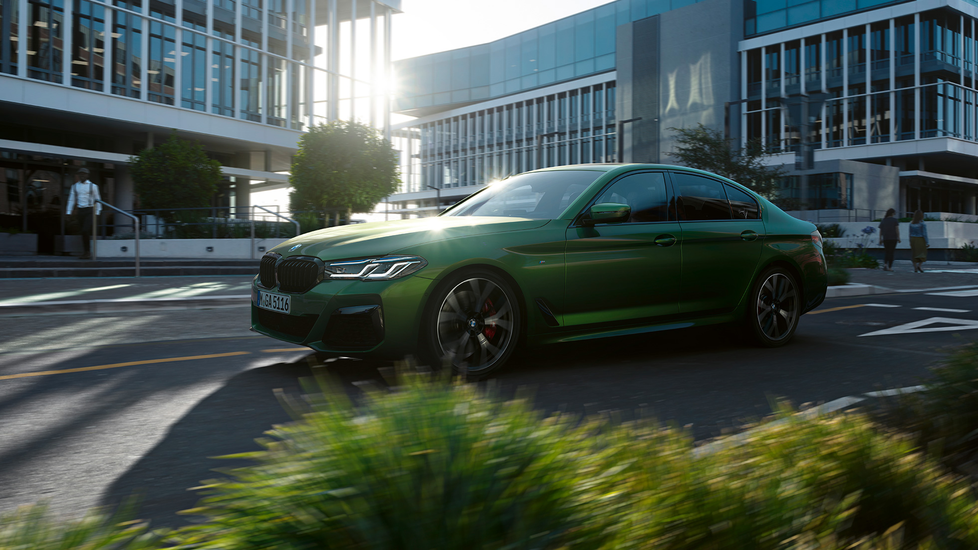 BMW M550i xDrive Седан G30 LCI 2020 вид на бічну частину під час руху BMW M550i xDrive Седан G30 LCI 2020 кольору BMW Individual Verde Ermes Metallic вид на бічну частину під час руху центром міста