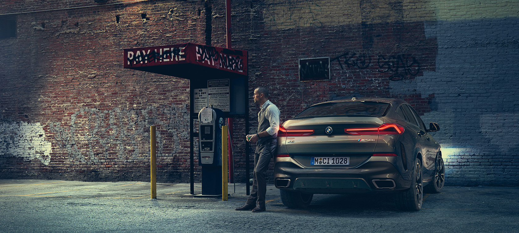 Задня частина BMW X6 M50i. Чоловік спирається на задню частину BMW X6 M50i.