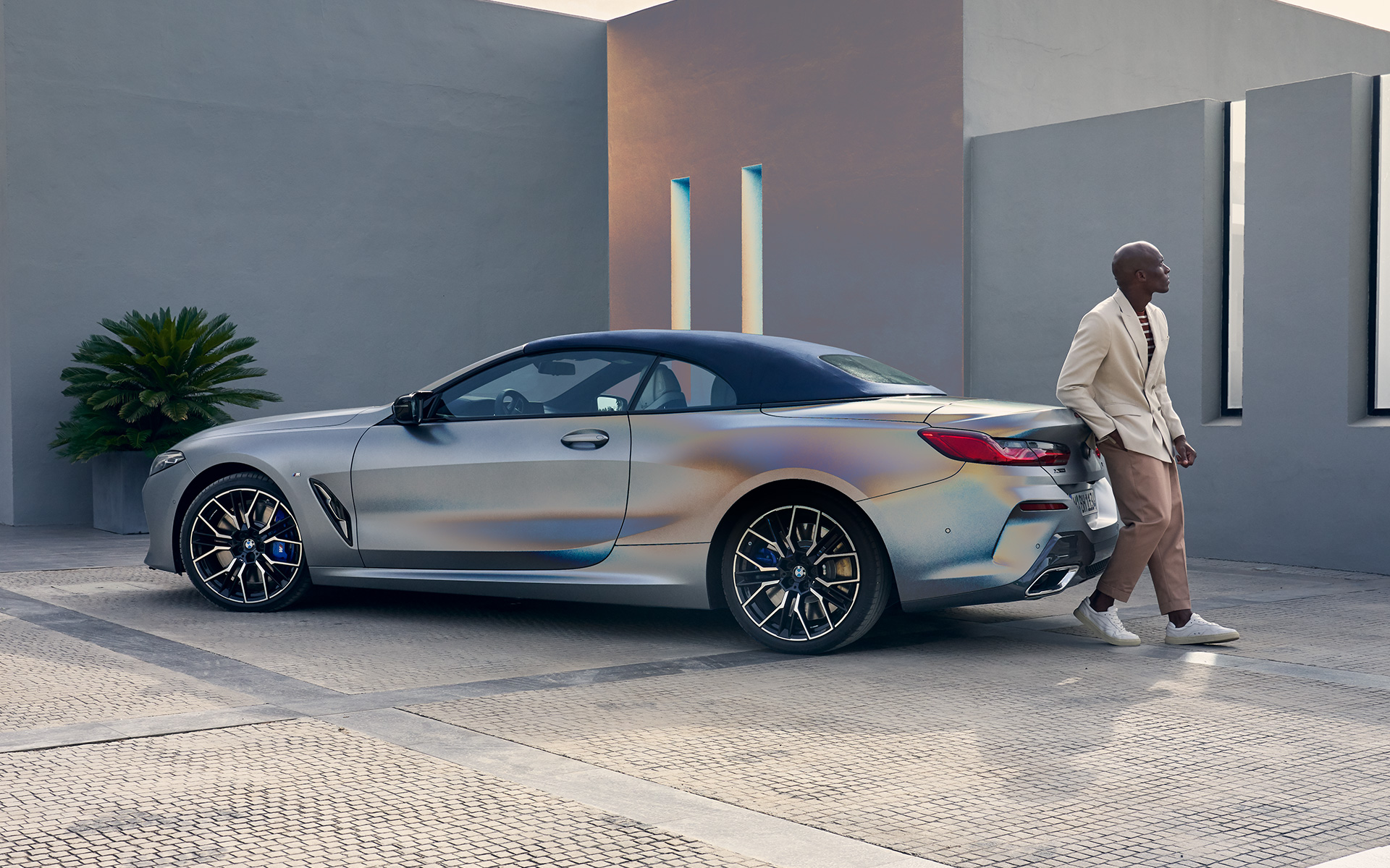 Вид ззаду на три чверті BMW M850i xDrive Cabrio G14 LCI Facelift 2022 BMW М850і xDrive Cabrio G14 LCI Facelift 2022 у кольорі BMW Individual Frozen Pure Grey metallic, вид ззаду на три чверті змоделлю, що спирається на автомобіль