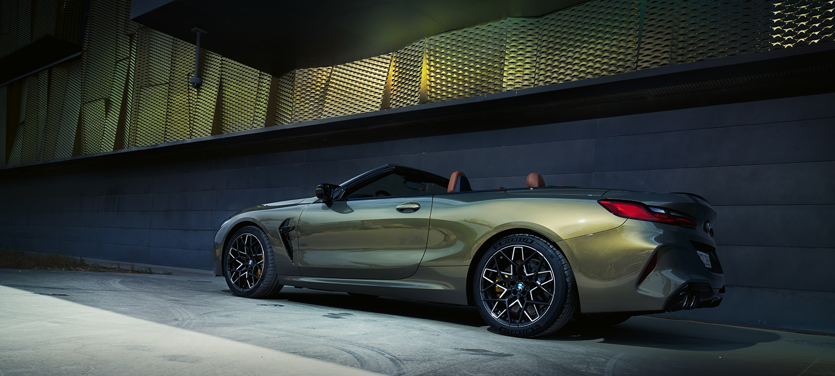 BMW M8 Cabrio F91 LCI Facelift 2022 у кольорі BMW Individual Brass metallic, вид збоку на три чверті на фоні стіни