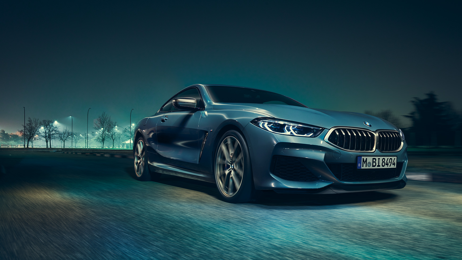 BMW M850i xDrive Coupé, вид спереду з поворотом в три чверті зліва. BMW M850i xDrive Coupé в Barcelona Blue металік, вид спереду з поворотом в три чверті зліва, їзда вночі.