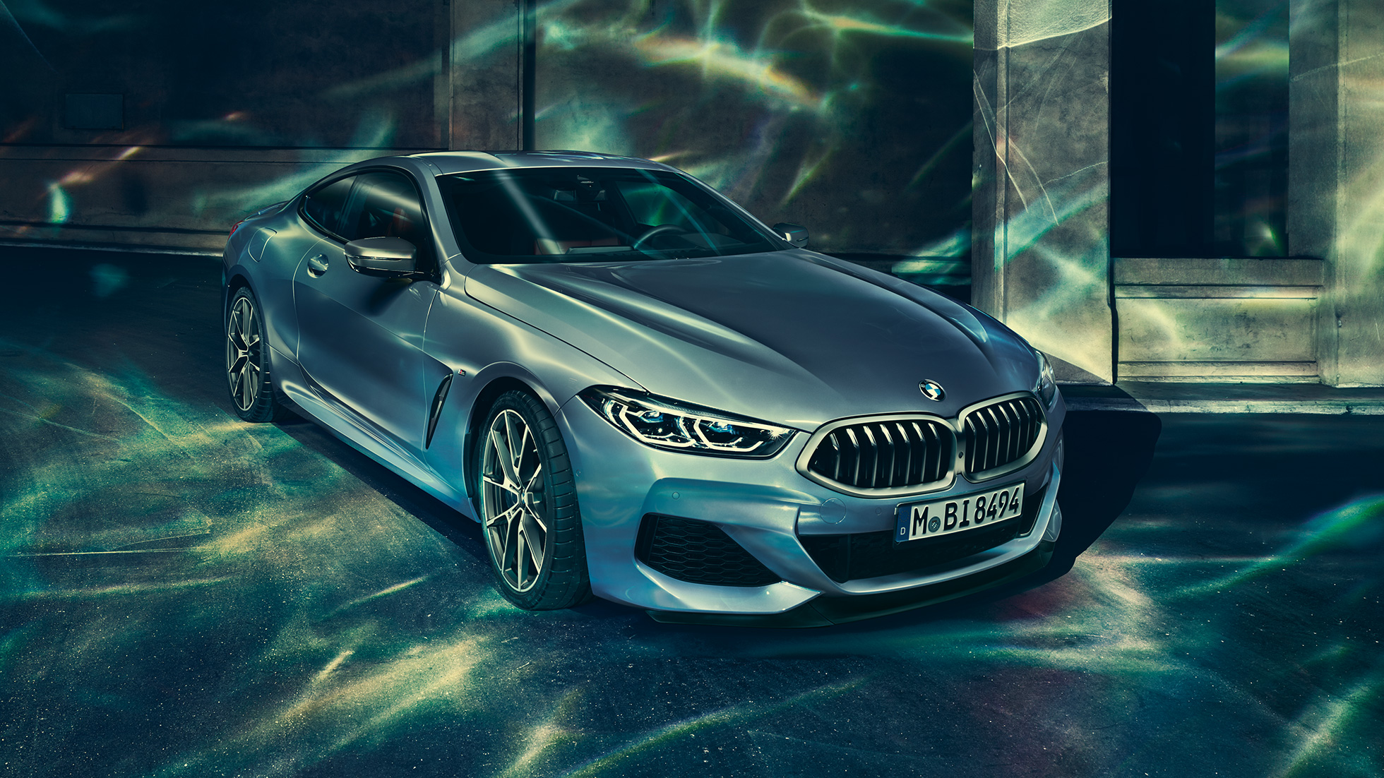 BMW M850i xDrive, вид спереду з поворотом в три чверті зліва. BMW M850i xDrive Coupé в Barcelona Blue металік, вид спереду з поворотом в три чверті зліва, стоїть перед будівлею.