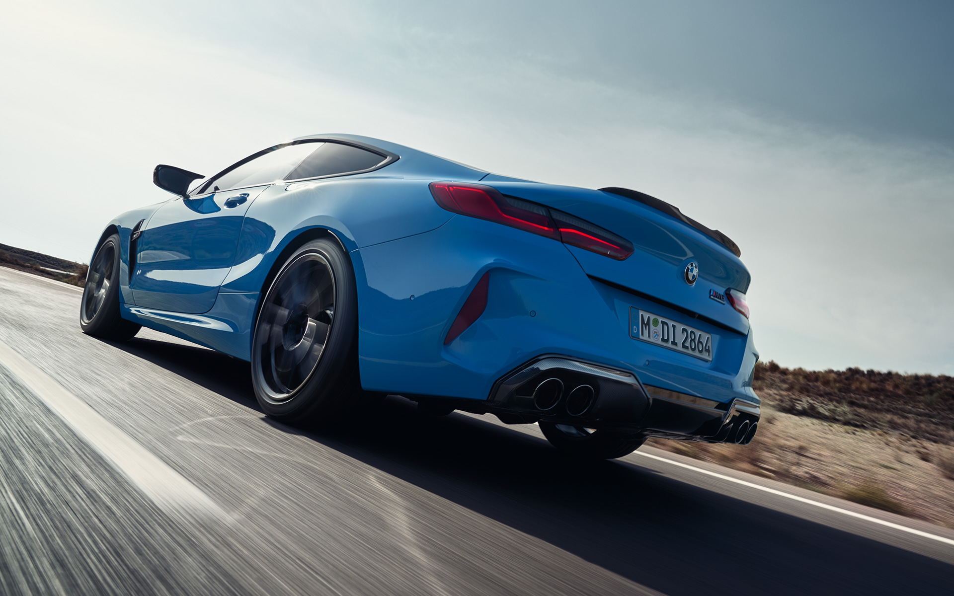 BMW M8 Competition Coupe F92 LCI 2022 вид ззаду на три чверті під час їзди BMW M8 Competition Coupe F92 LCI Facelift 2022 у кольорі BMW Individual Daytona Beach Blue, вид ззаду на три чверті під час руху на шосе