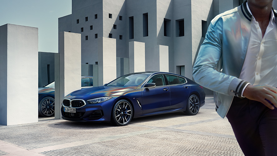 BMW M850i xDrive Gran Coupe G16 LCI Facelift 2022 BMW Individual у кольорі Frozen Tanzanite Blue metallic, вид спереду на три чверті статичний з моделлю в кадрі