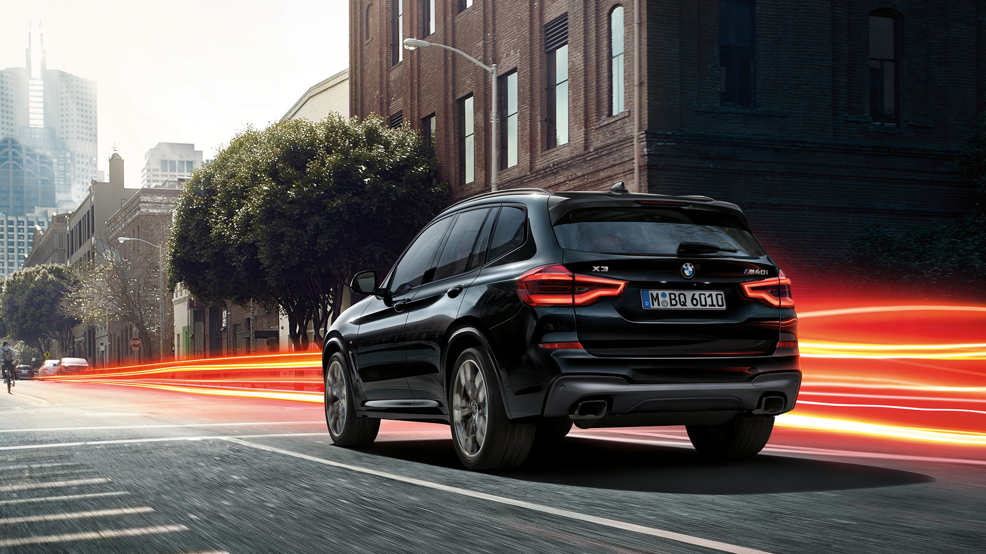 BMW X3 M40i в Black Sapphire, вид ззаду з поворотом в три чверті. BMW X3 M40i в Black Sapphire металік, за кермом, екстер'єр, вид ззаду з поворотом в три чверті на міському тлі зі світловими смужками.