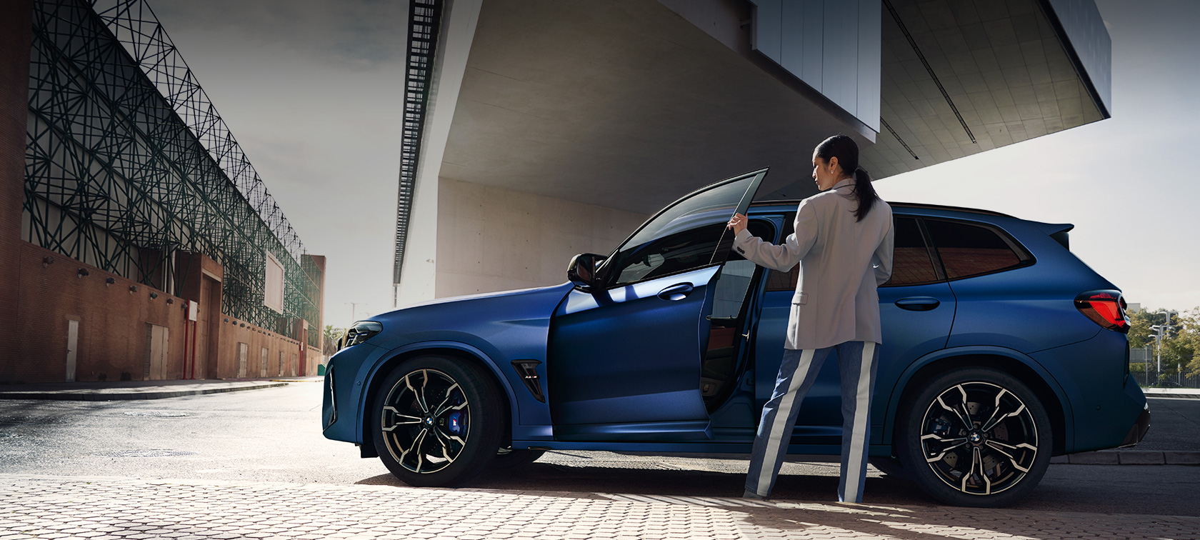 BMW X3 M Competition F97 LCI Facelift 2021, вид збоку на місці BMW X3 M Competition F97 LCI Facelift 2021 в кольорі BMW Individual Frozen Portimao Blue металік, вид збоку з відкритими дверима і жіночої моделлю
