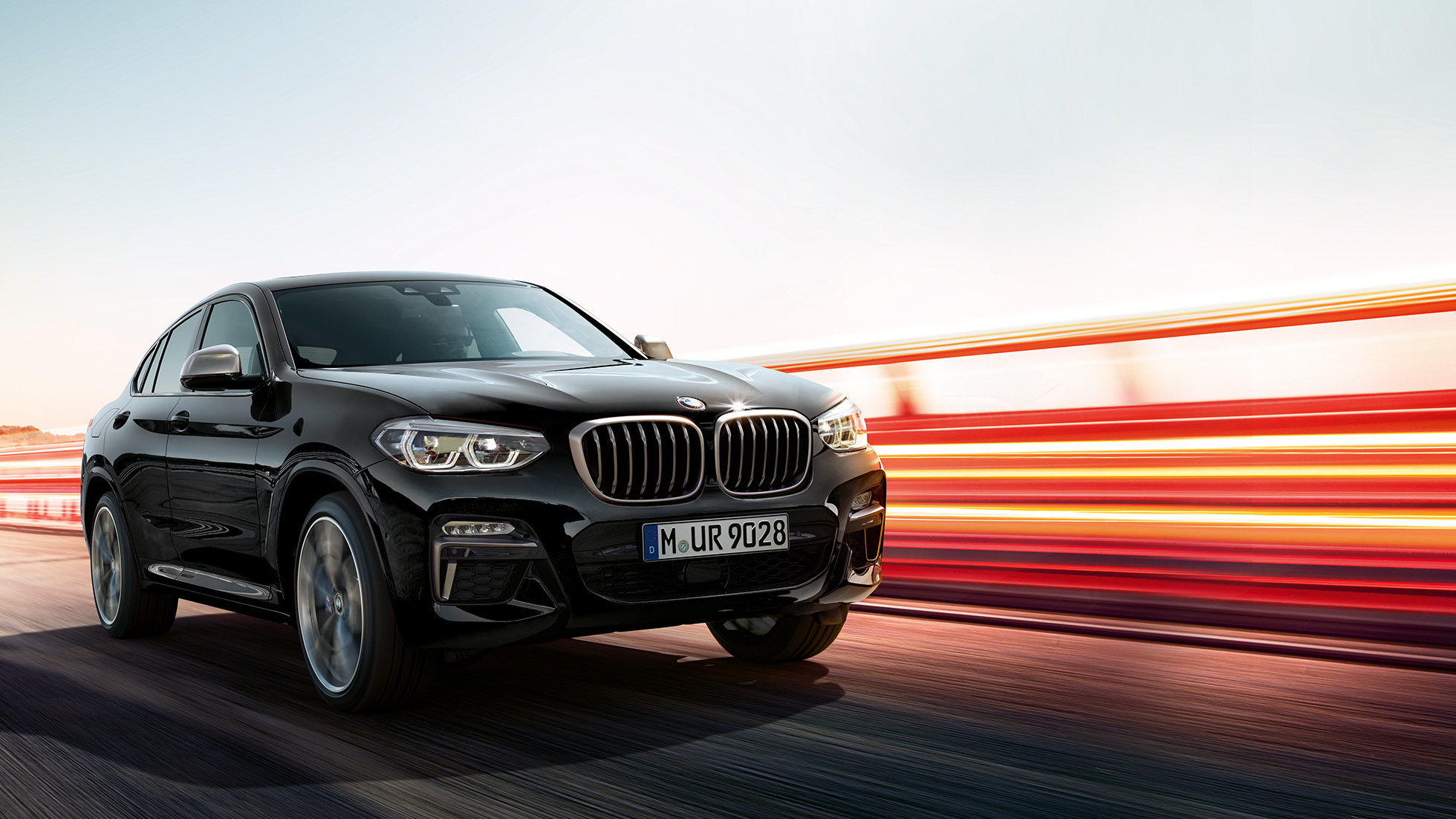 BMW X4 M40i, вид сзади с поворотом в три четверти. BMW X4 M40i в Black Sapphire металлик, за рулем, экстерьер, вид сзади с поворотом в три четверти со световыми полосками.