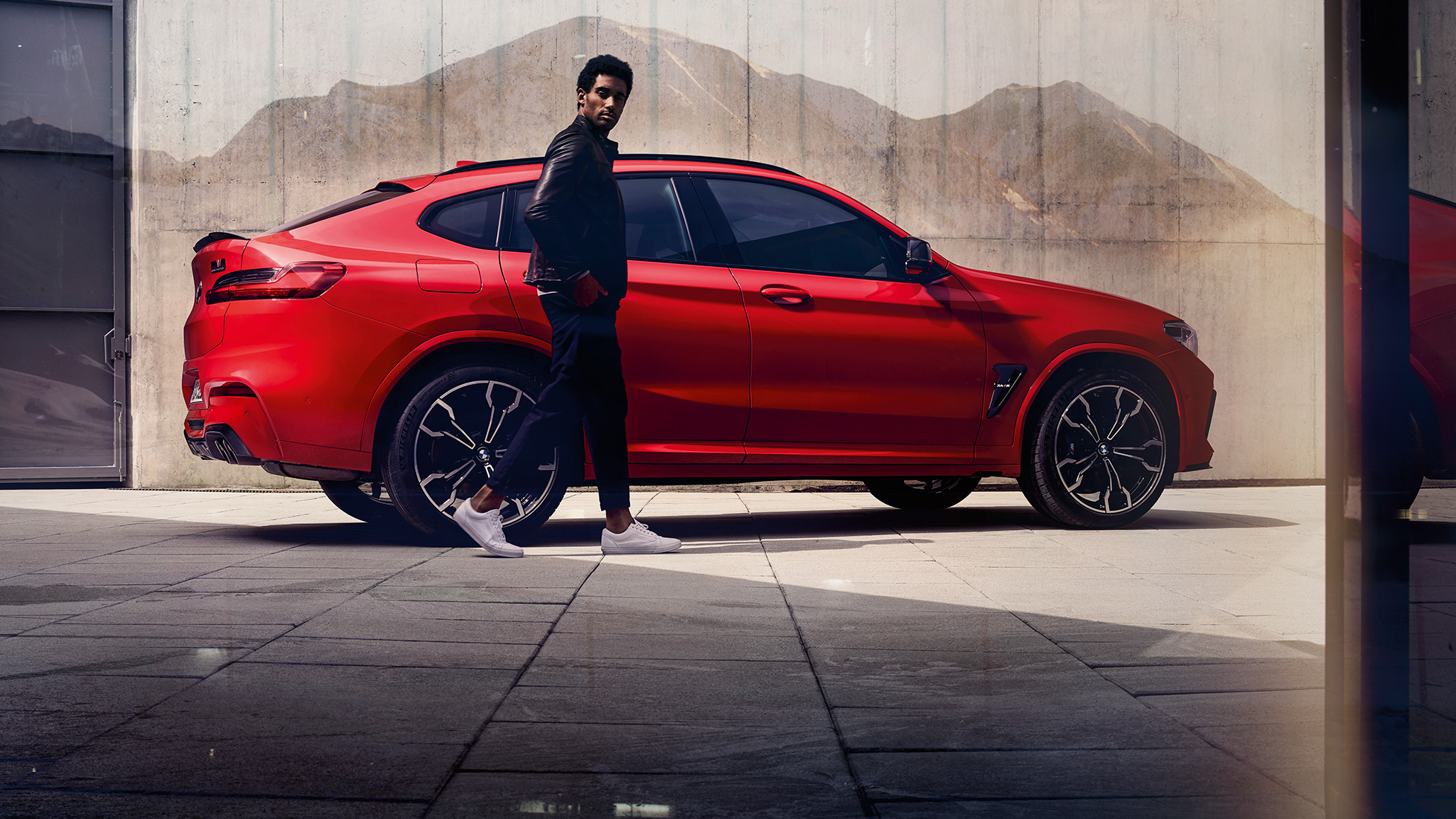 BMW X4 M Competition, вид сбоку с молодым человеком. BMW X4 M Competition в Toronto Red металлик, экстерьер, вид сбоку с молодым человеком.