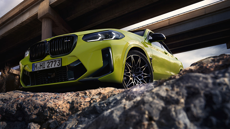 BMW X4 M Competition F98 LCI Facelift 2021 кольорі Sao Paulo Yellow, вид спереду в три чверті з видом знизу проїжджаючи під мостом