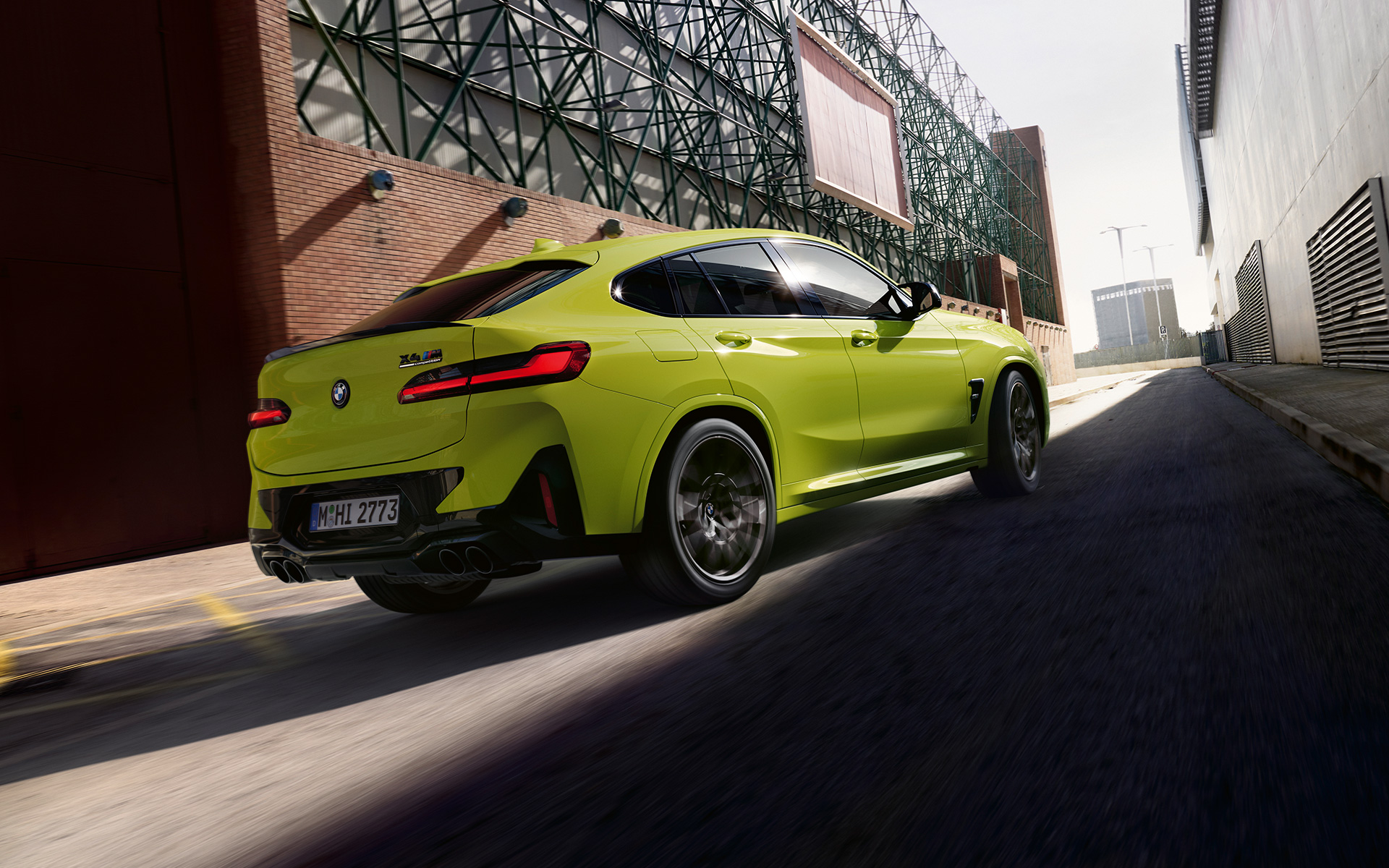 BMW X4 M Competition F98 LCI Facelift 2021 в кольорі Sao Paulo Yellow, вид спереду в три чверті проїжджаючи між фабричними будівлями