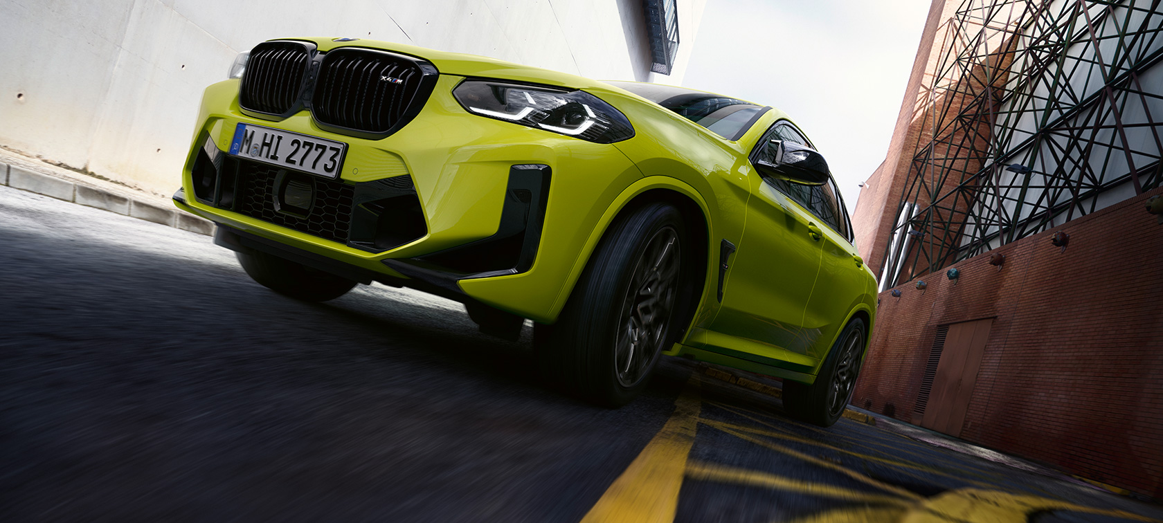 BMW X4 M Competition F98 LCI Facelift 2021 в кольорі Sao Paulo Yellow, вид спереду в три чверті з видом знизу проїжджаючи через сектор будинків