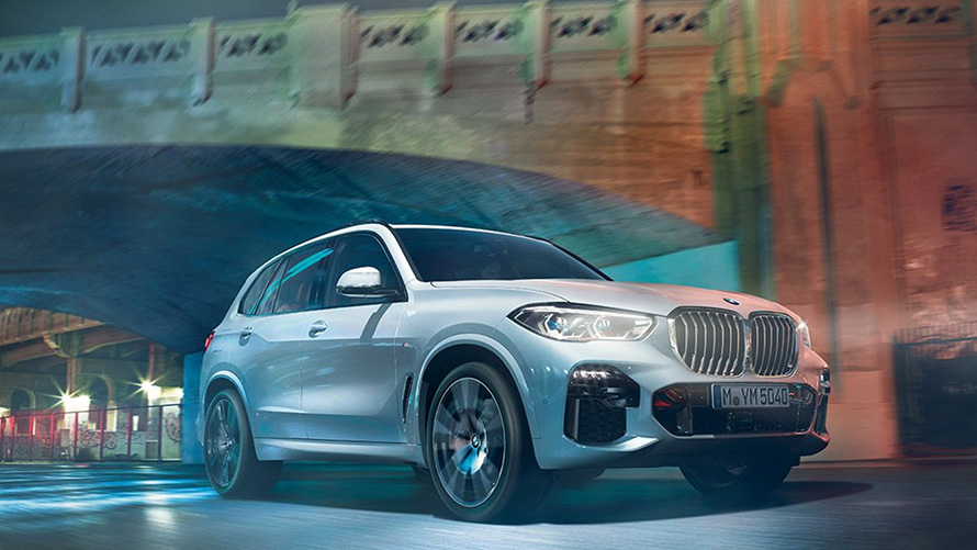 BMW X5 вид спереду в три чверті G05 Позашляховик BMW Х5 G05 2018 у кольорі Mineral White металік, вид в три чверті спереду під час руху в нічний час