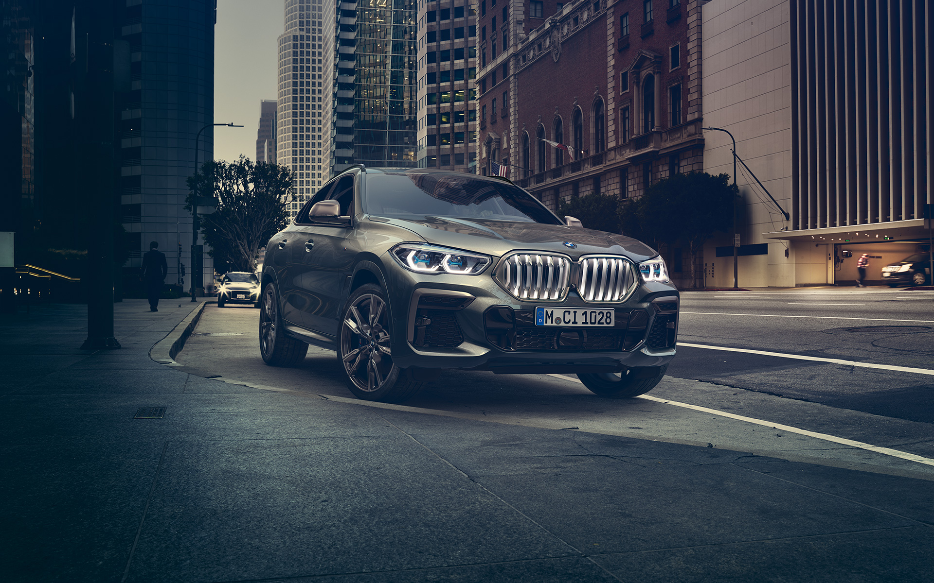 BMW X6 M50i у передній перспективі в три чверті, що стоїть перед міським пейзажем G06 2018 SUV