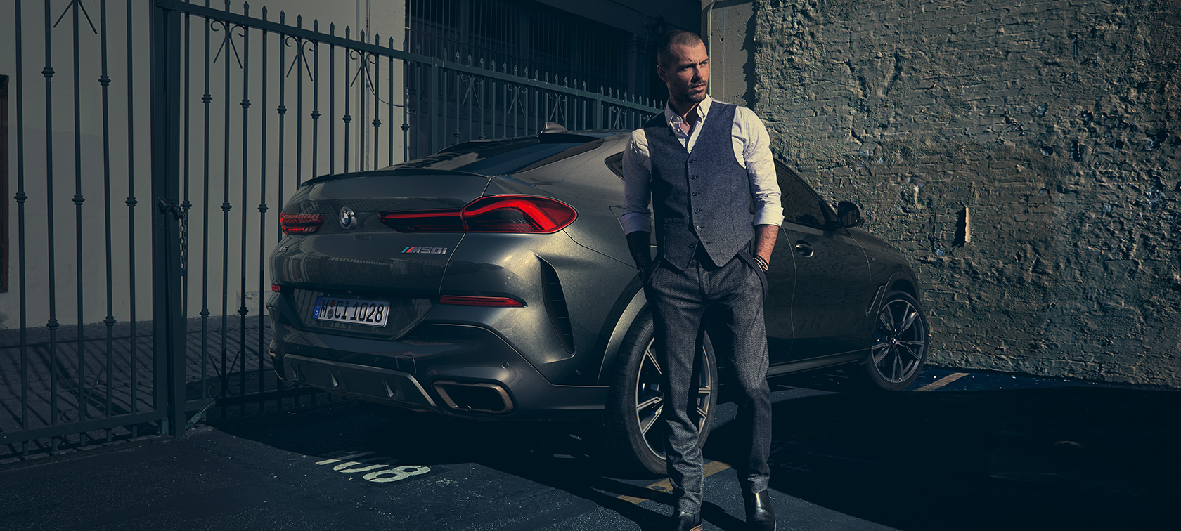 BMW X6 M50i вид ззаду в три чверті G06 Чоловік стоїть поруч із позашляховиком BMW X6 M50i G06 2018 вид ззаду в три чверті